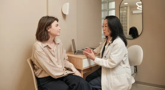 Female dentist in white coat consulting with patient in dental office reception area.