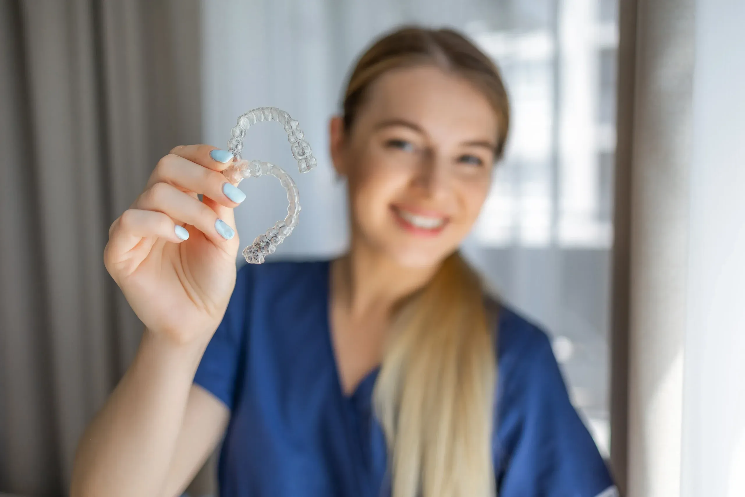Smiling dental professional holding clear aligners in a bright room